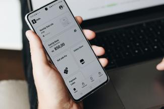 A person holding a cell phone in front of a laptop by SumUp courtesy of Unsplash.